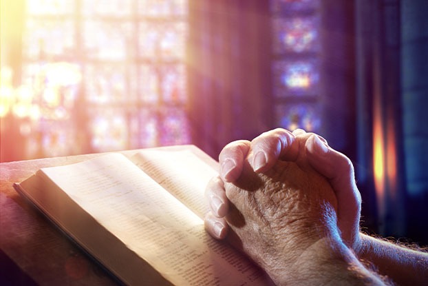 Mãos em cima de uma Blíblia com vitral embaçado atrás