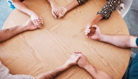 Business people holding hands in therapy group, team building or staff support with diversity, empathy and solidarity. Corporate circle hand holding on table above for prayer, trust and community